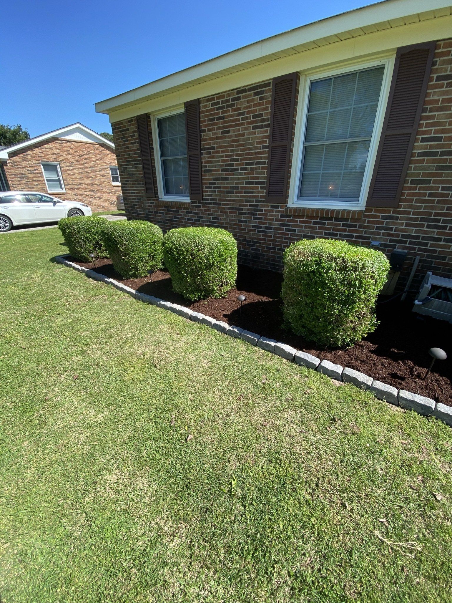 A brick house with a lush green lawn and bushes in front of it.