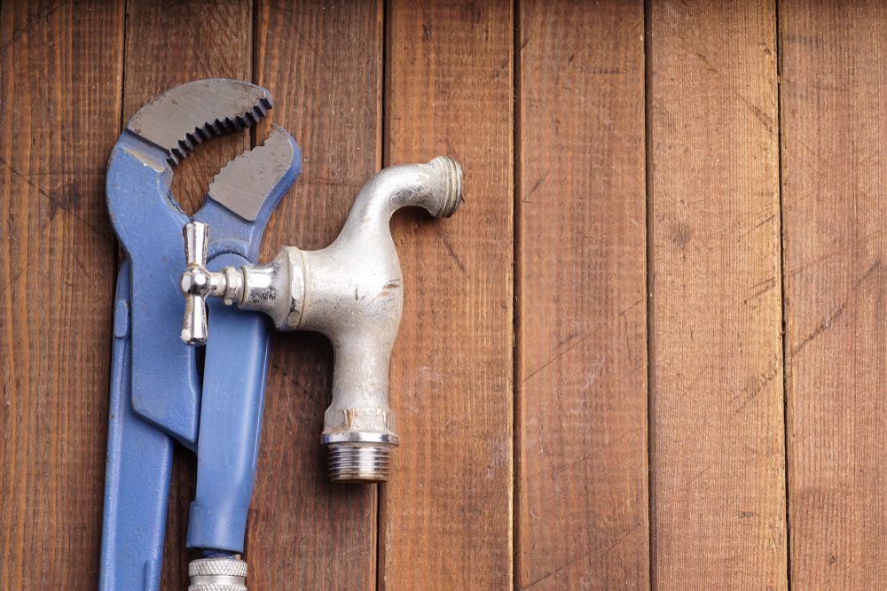 A Faucet And A Wrench Are Sitting On A Wooden Table — H2O Plumbing & Maintenance Services In Armidale, NSW