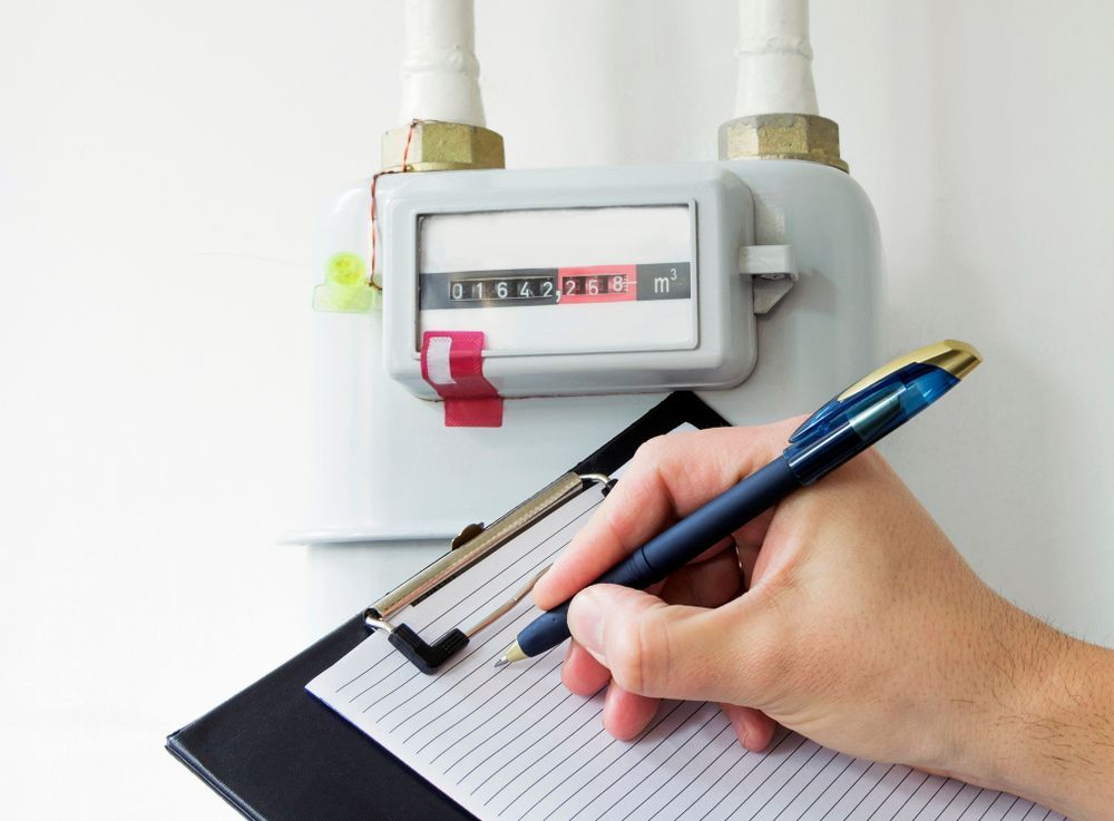 A Person Is Writing On A Clipboard In Front Of A Gas Meter — H2O Plumbing & Maintenance Services In Armidale, NSW