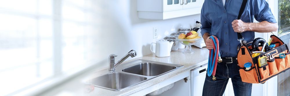 A Plumber Is Standing In A Kitchen Holding A Tool Bag — H2O Plumbing & Maintenance Services In Armidale, NSW