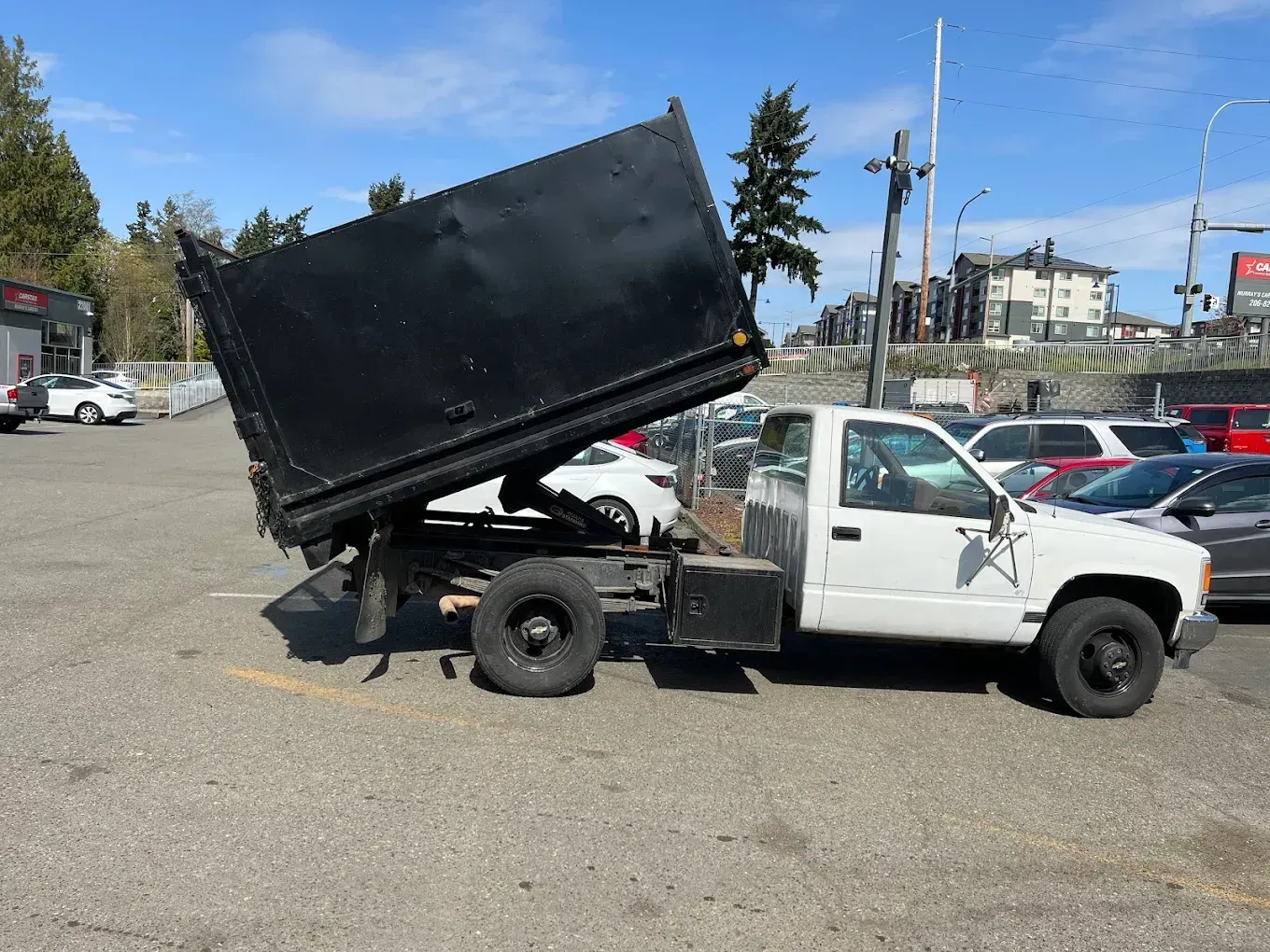 White dump truck with raised black bed parked in an open lot under a blue sky.