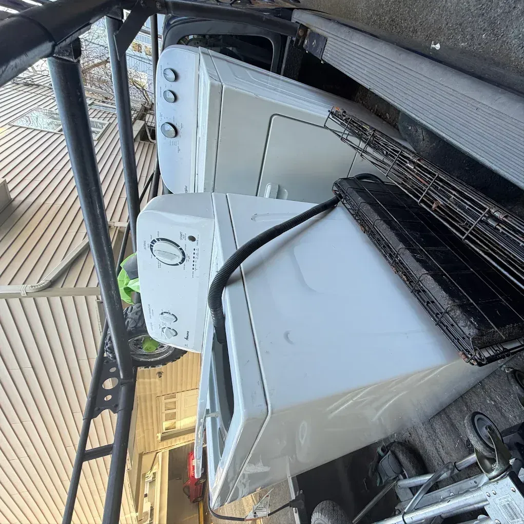 Two white appliances, a washer and dryer, stacked outdoors beside a building wall.