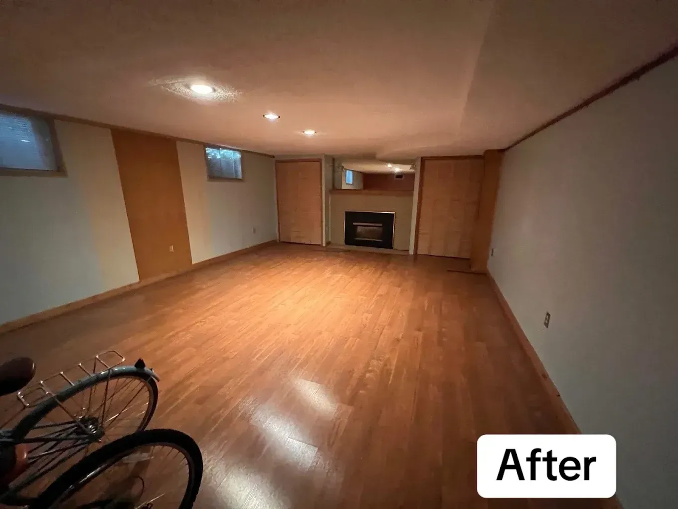 Empty finished basement with wood floors, recessed lights, and a fireplace in the back wall.
