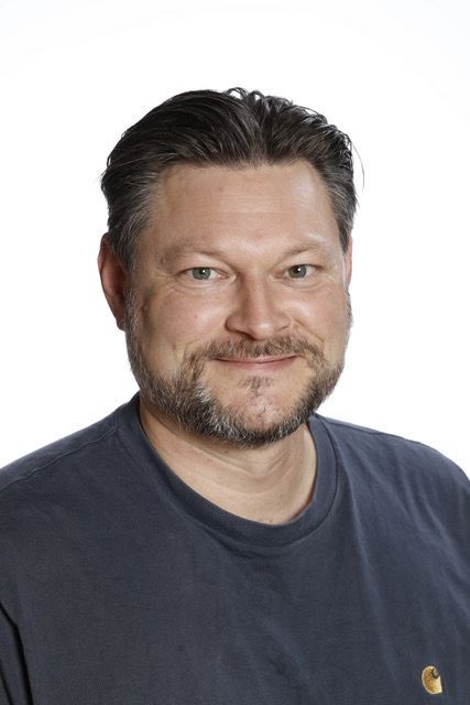 En mand med skæg har en blå sweater på og smiler til kameraet.