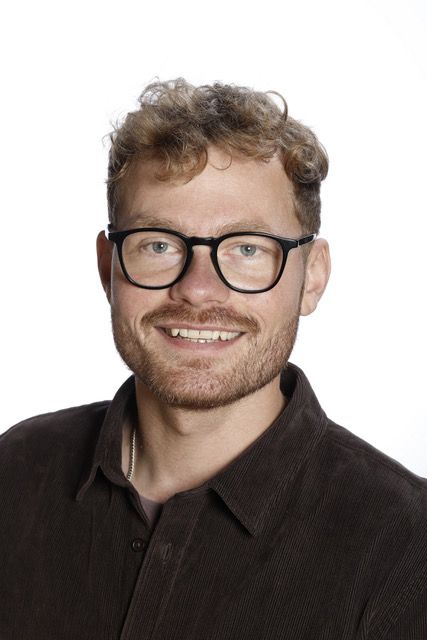 En mand med briller og skæg smiler til kameraet.