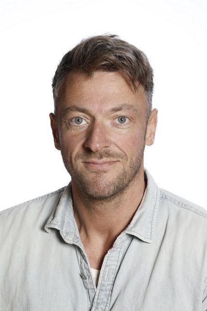 En mand i en sort skjorte står foran en hvid baggrund.