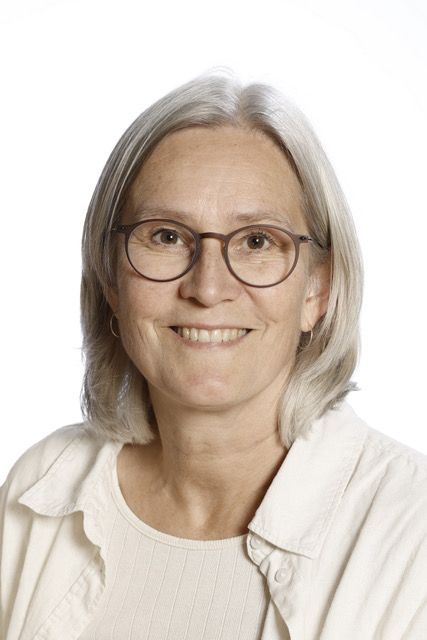 En kvinde med briller og jakke smiler til kameraet.