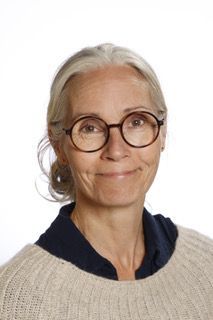 En kvinde med briller og sweater smiler til kameraet.