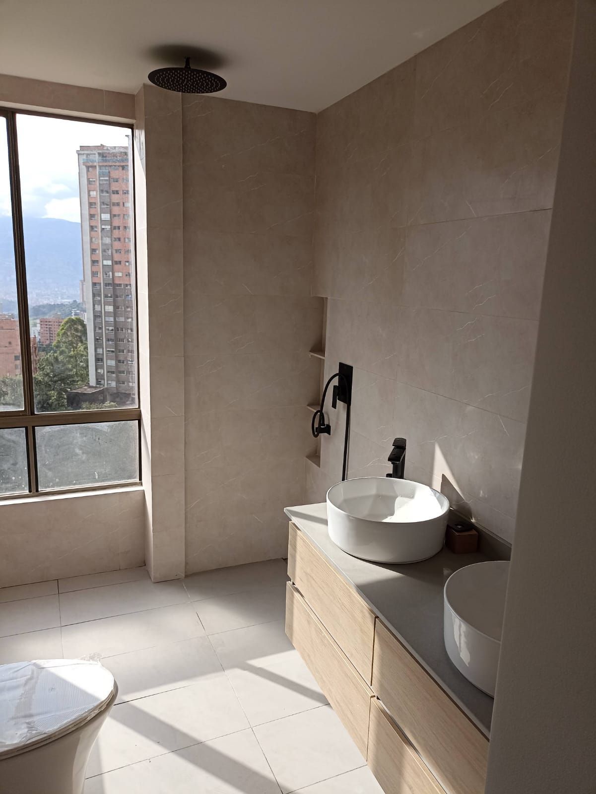 Baño moderno con lavabos dobles, ventana grande y vista a la ciudad.