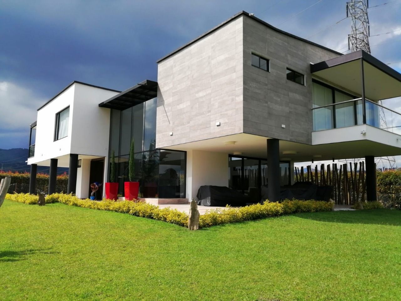 Casa moderna con exterior blanco y gris, grandes ventanales y un césped verde bajo un cielo azul.