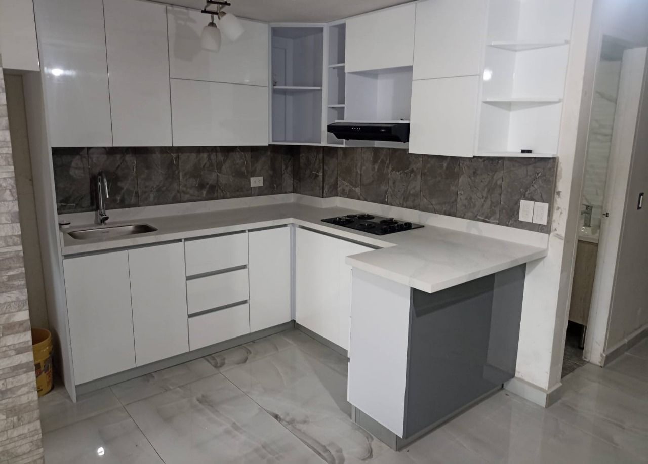 Cocina moderna blanca en forma de L con salpicadero gris, suelo de baldosas y banco con isla central.