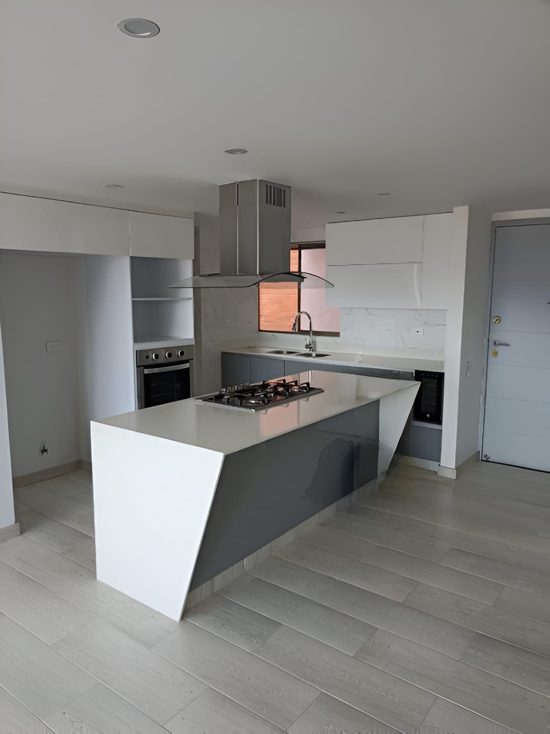 Cocina moderna con isla blanca, armarios grises y suelos de madera clara.