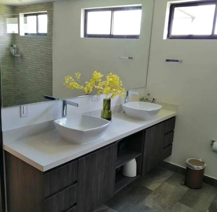 Tocador de baño moderno con dos lavabos sobre encimera, espejos y un jarrón con flores amarillas.
