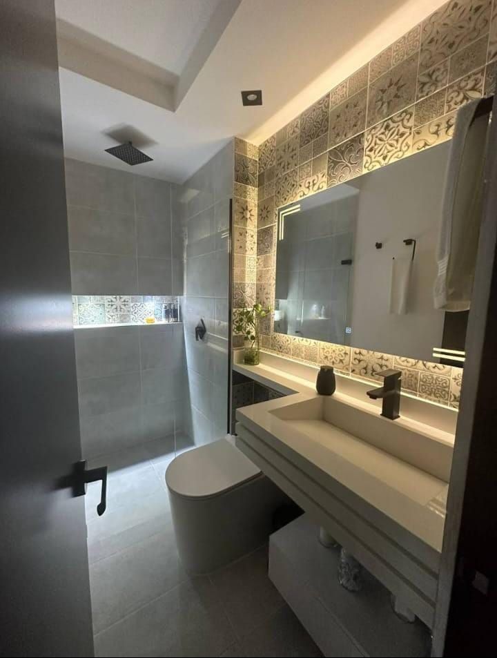 Baño moderno con tonos grises, lavabo suspendido, espejo grande y mampara de ducha de vidrio esmerilado.