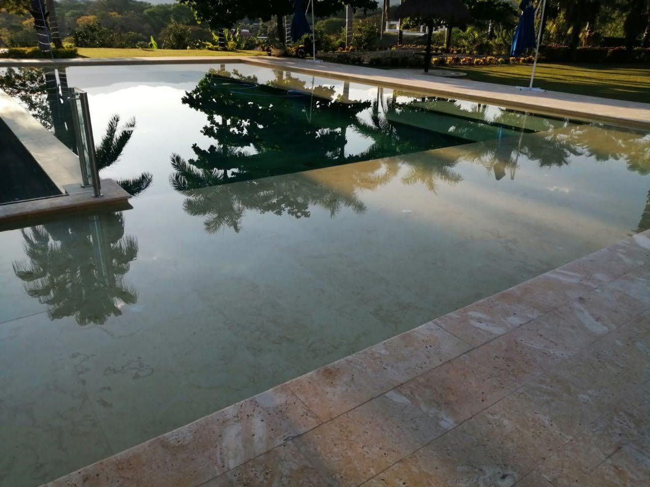 Estanque reflectante con agua tranquila, borde de piedra y reflejos de árboles en un parque.