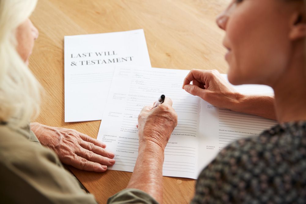 Two Women Are Sitting at a Table Signing a Last Will and Testament — Pollock Ingram Solicitors In Caloundra, QLD