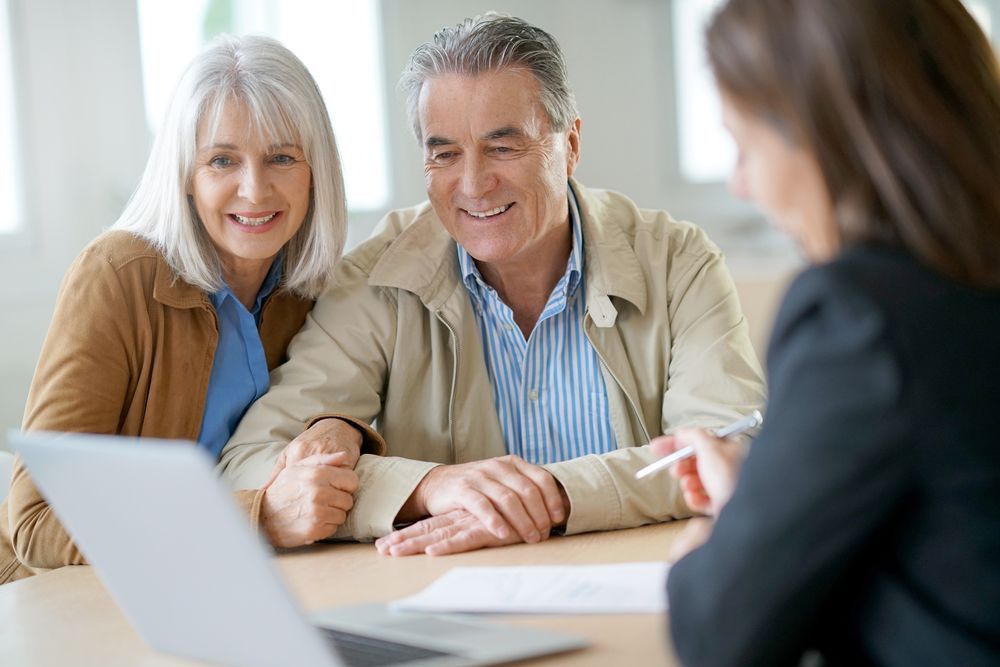 An older couple is sitting at a table talking to a man. — Pollock Ingram Solicitors In Caloundra, QLD