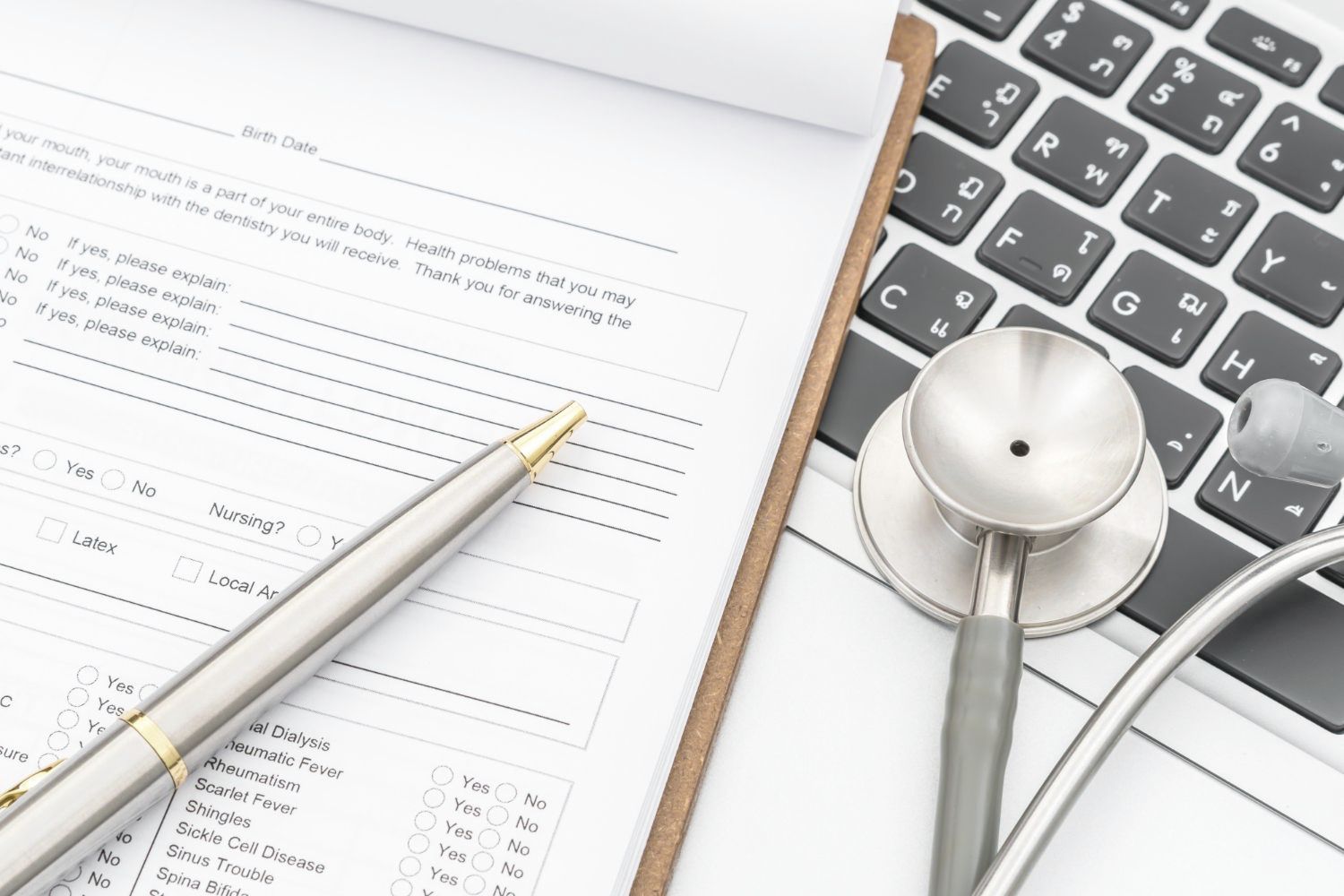 A stethoscope is sitting on top of a clipboard next to a laptop.