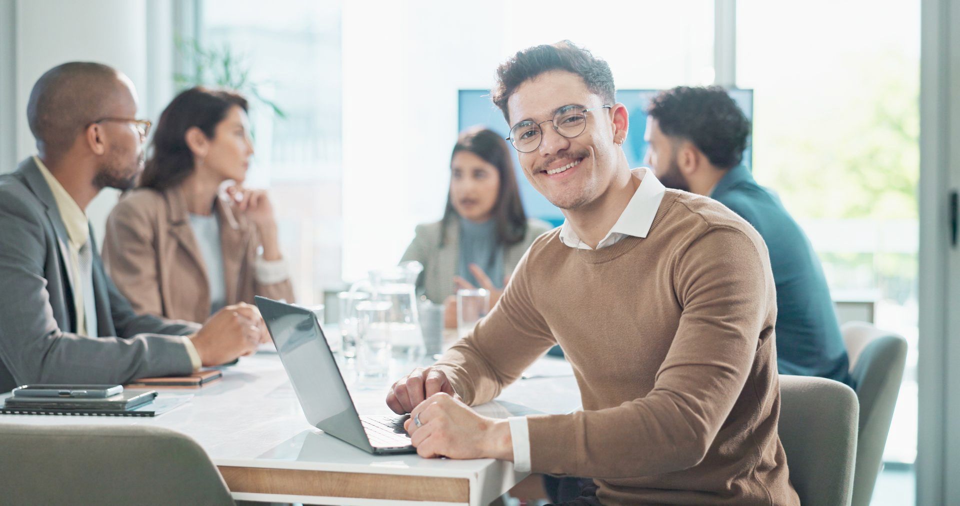 A man is sitting at a table with a laptop in front of a group of people.