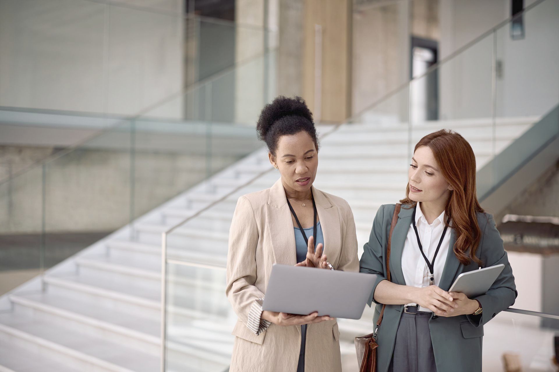 Two women are standing next to each other looking at a laptop.