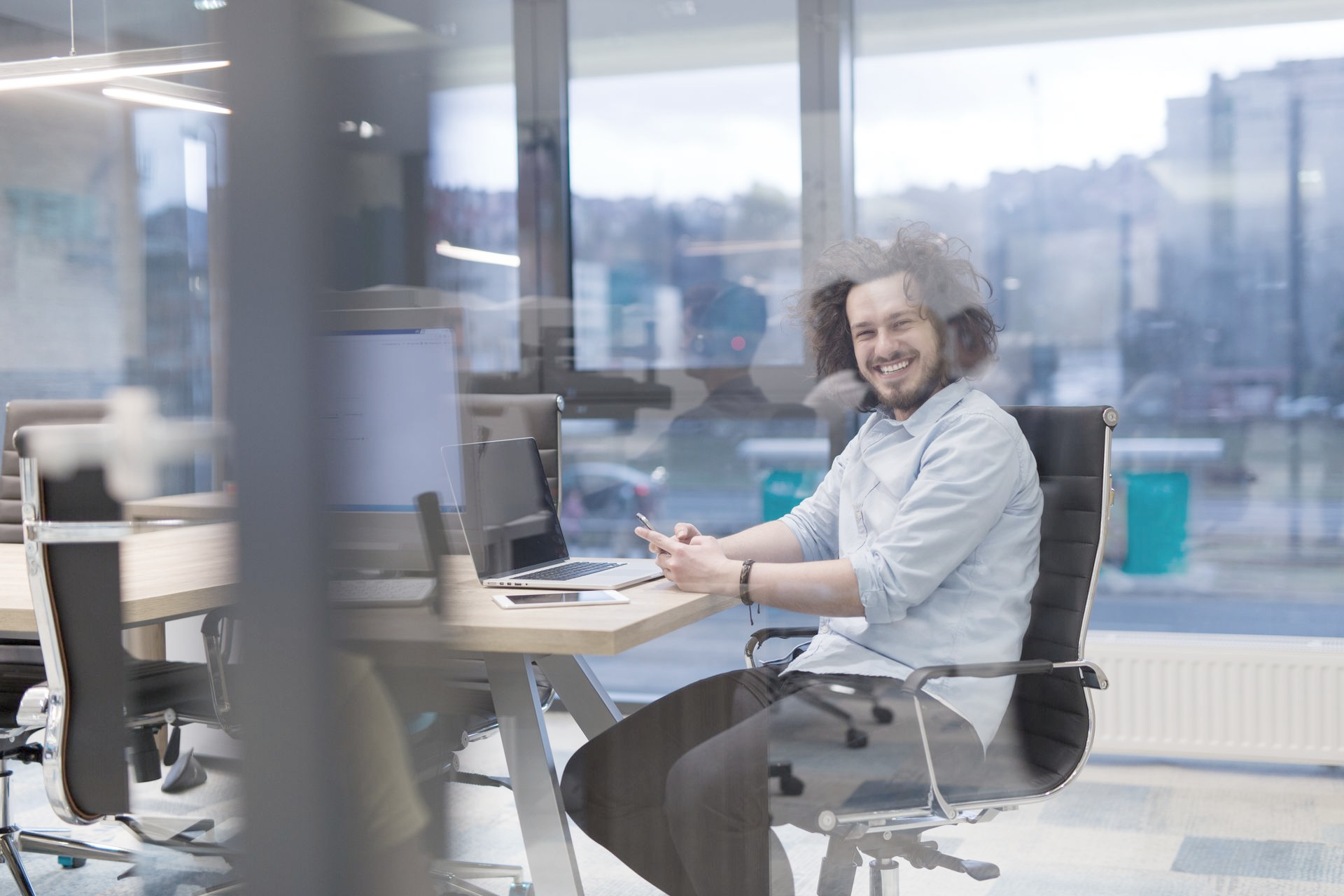 Man with curly hair smiles while sitting at a desk in an office.