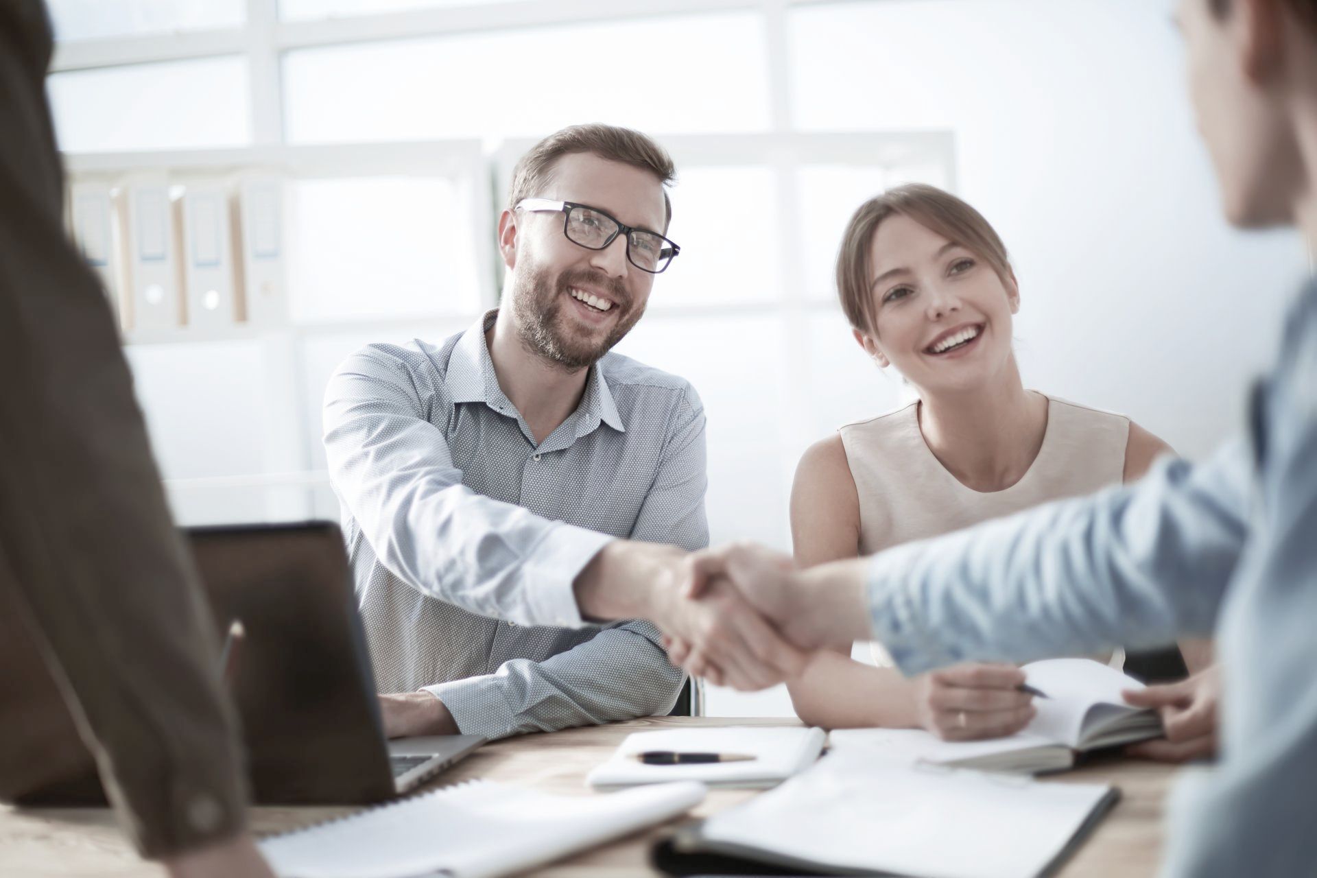 A man and a woman are shaking hands while sitting at a table.