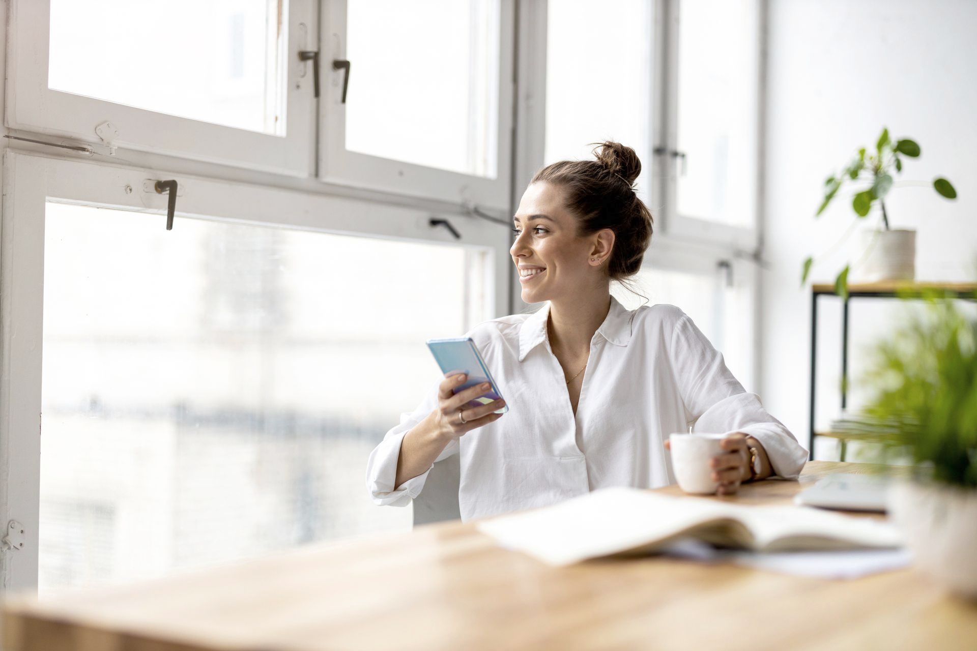 A woman is sitting at a table with a cup of coffee and a cell phone.