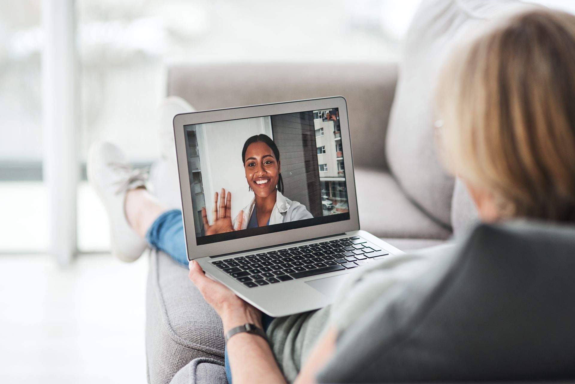Woman on a couch video-chatting with a doctor on a laptop, indoor setting.