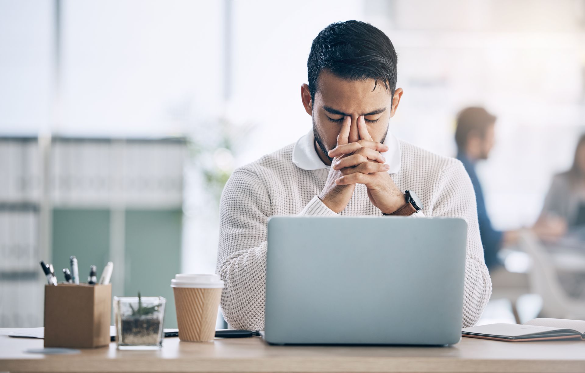 Person sitting at a desk, looking worried with hands clasped in front of a laptop in an office