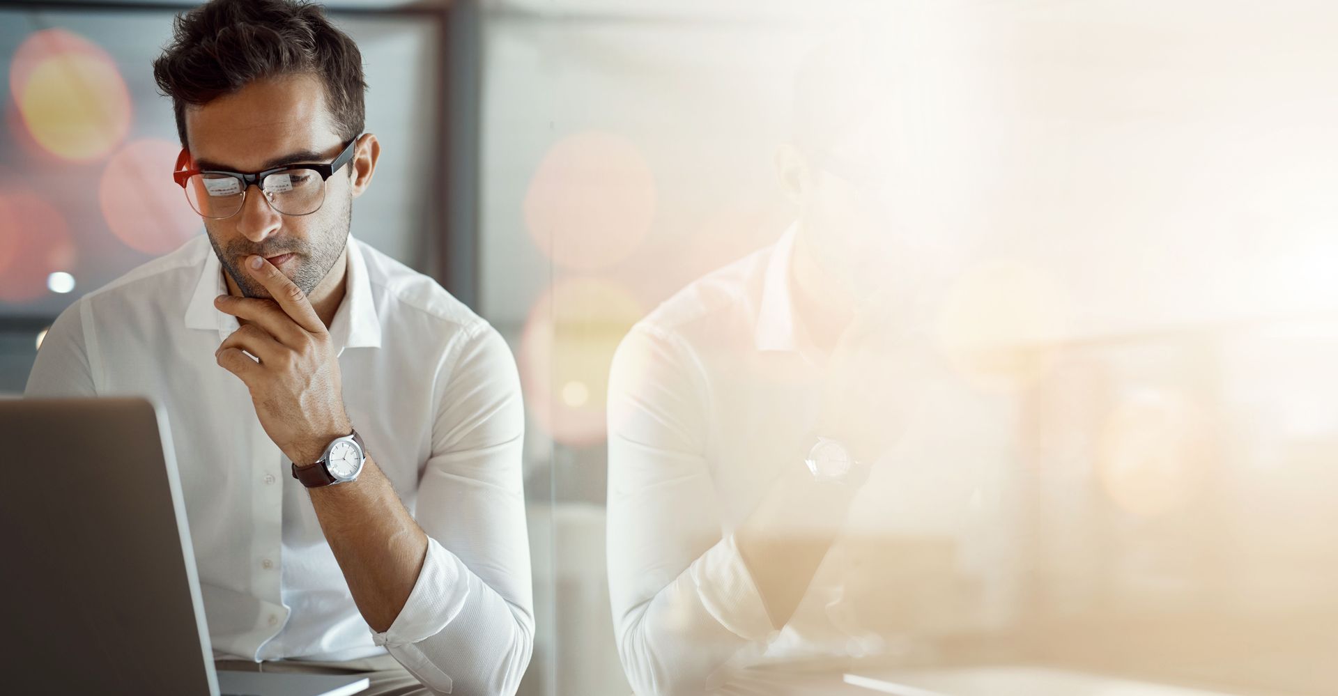 A man wearing glasses is sitting in front of a laptop computer.