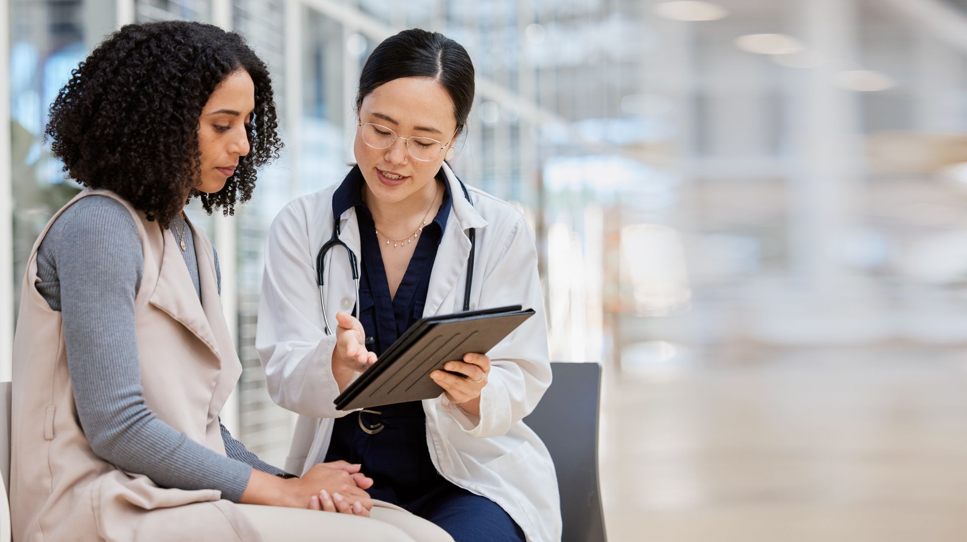 A professional in a white coat shows information on a tablet to a patient in a medical facility.