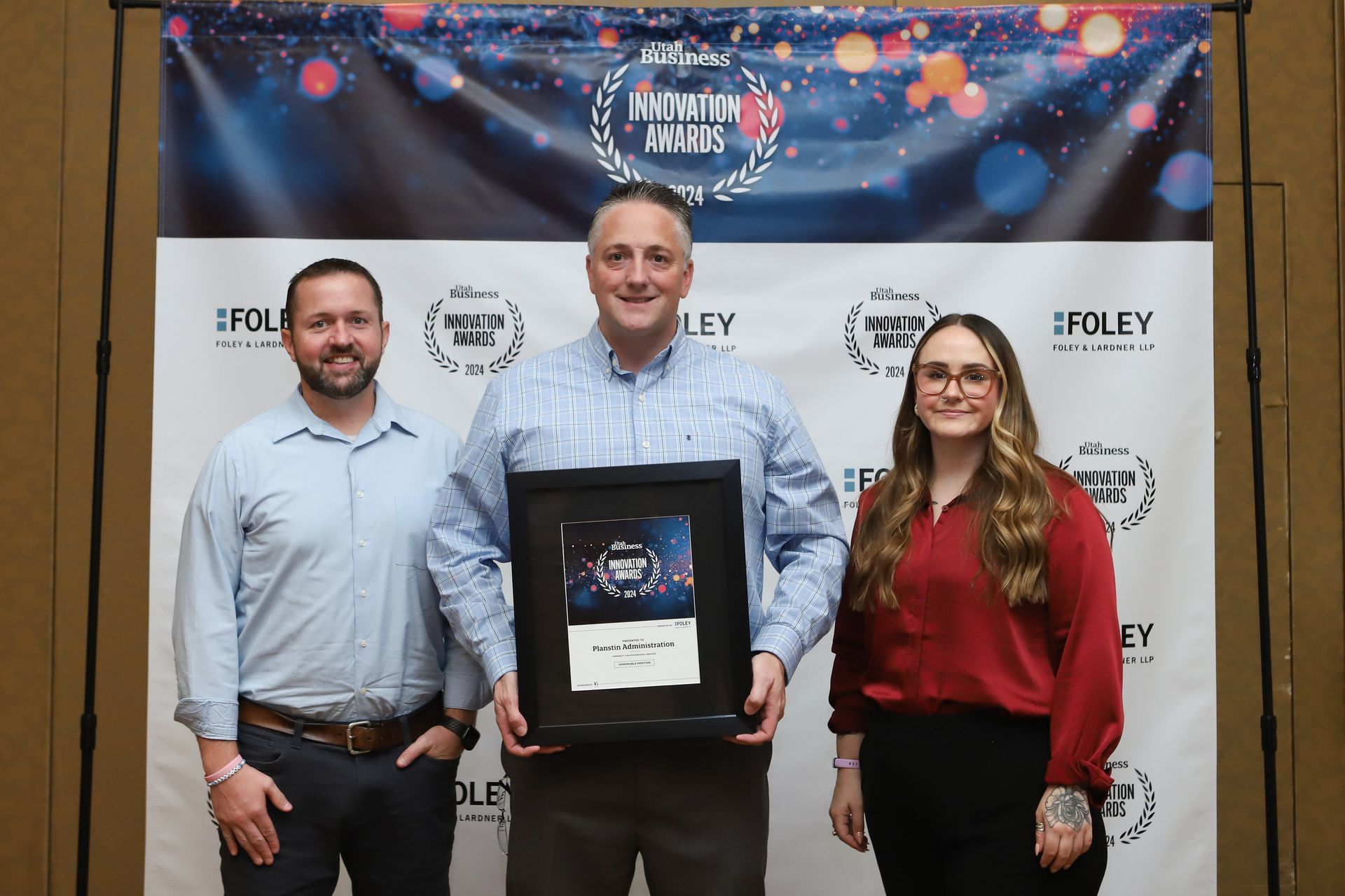 A man and two women are standing next to each other holding a framed award.