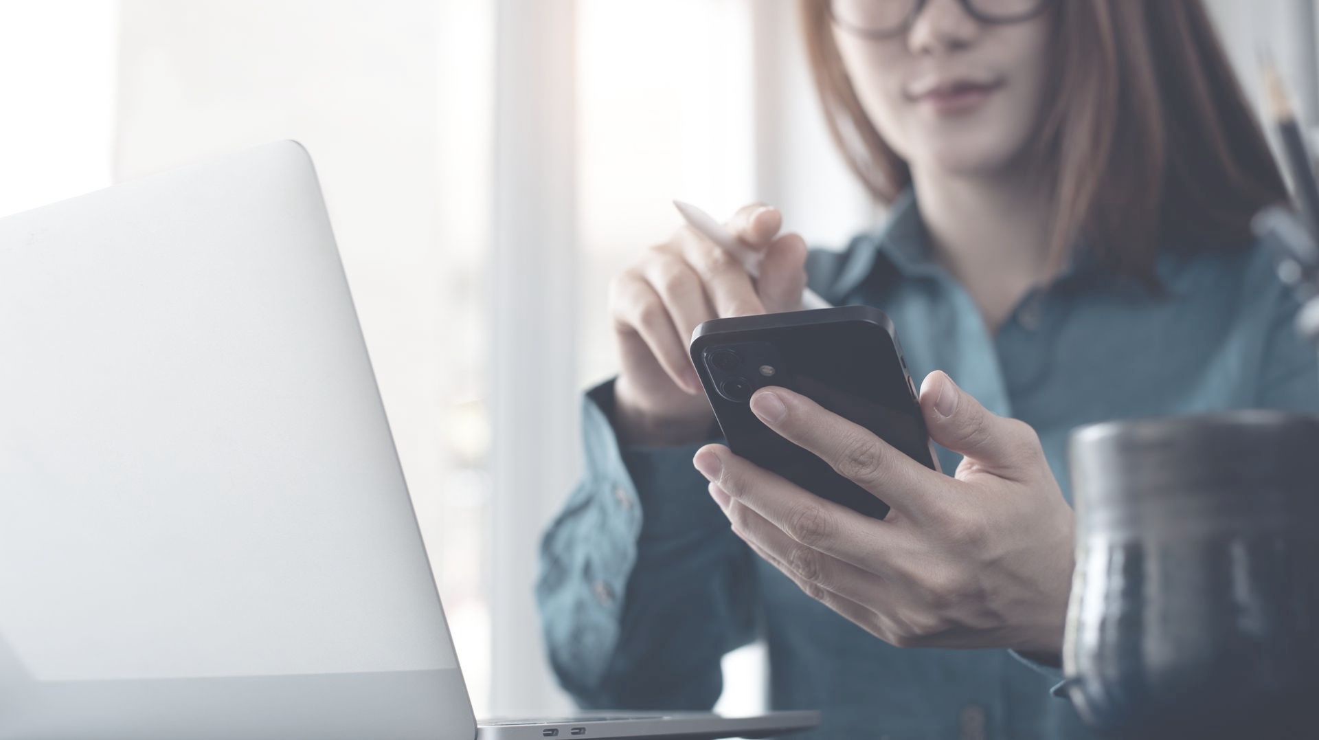 A woman is sitting at a table using a laptop and a cell phone.