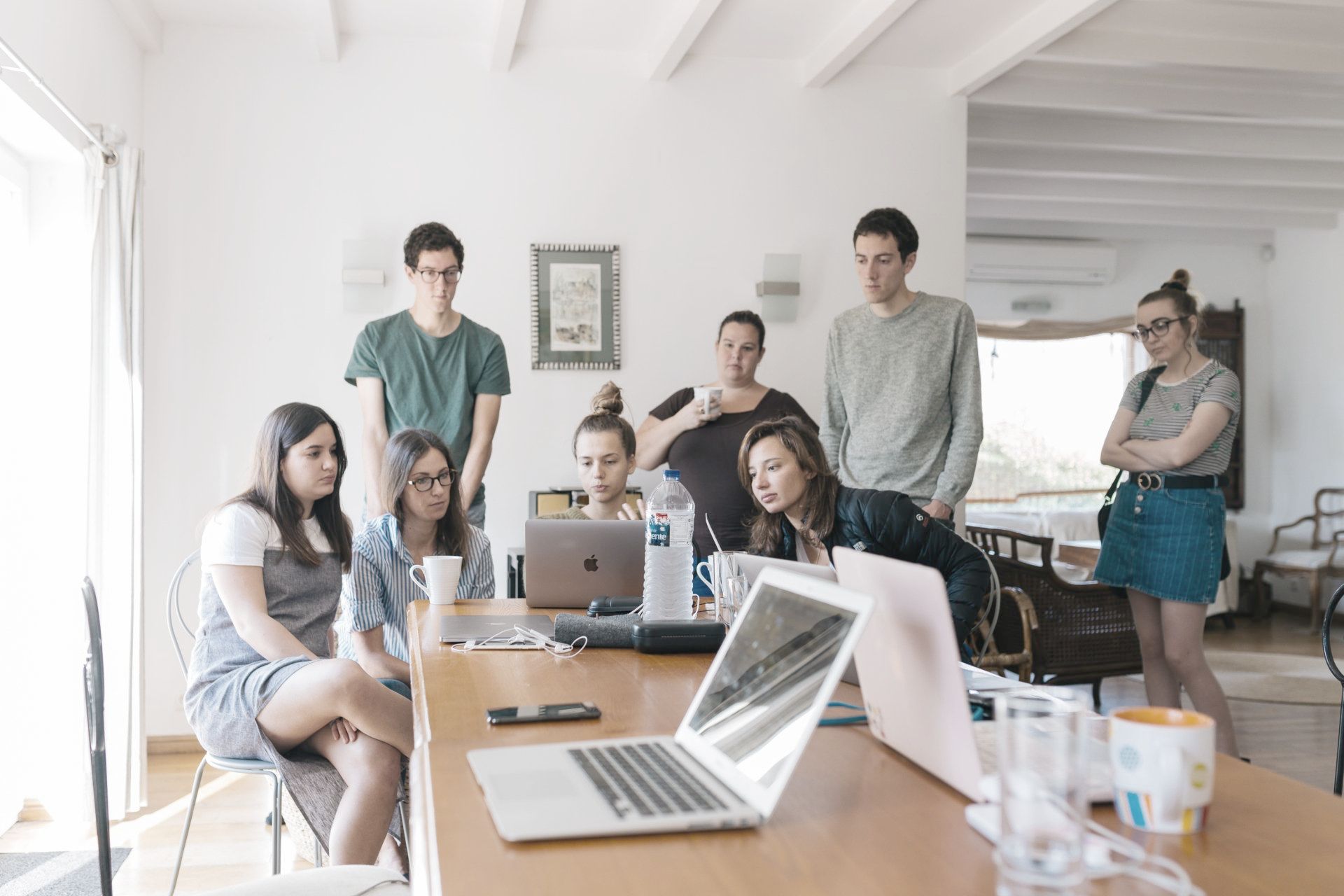 A group of people are sitting around a table with laptops.