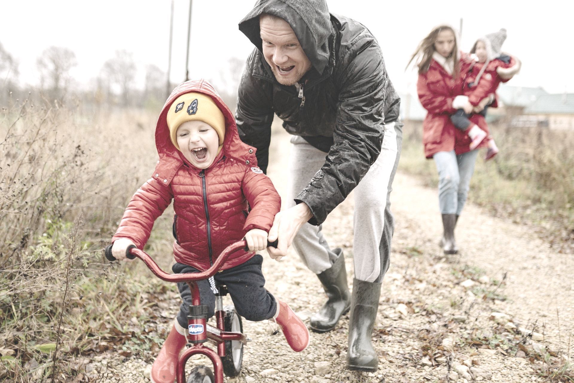 A man is helping a little boy ride a tricycle on a dirt road.