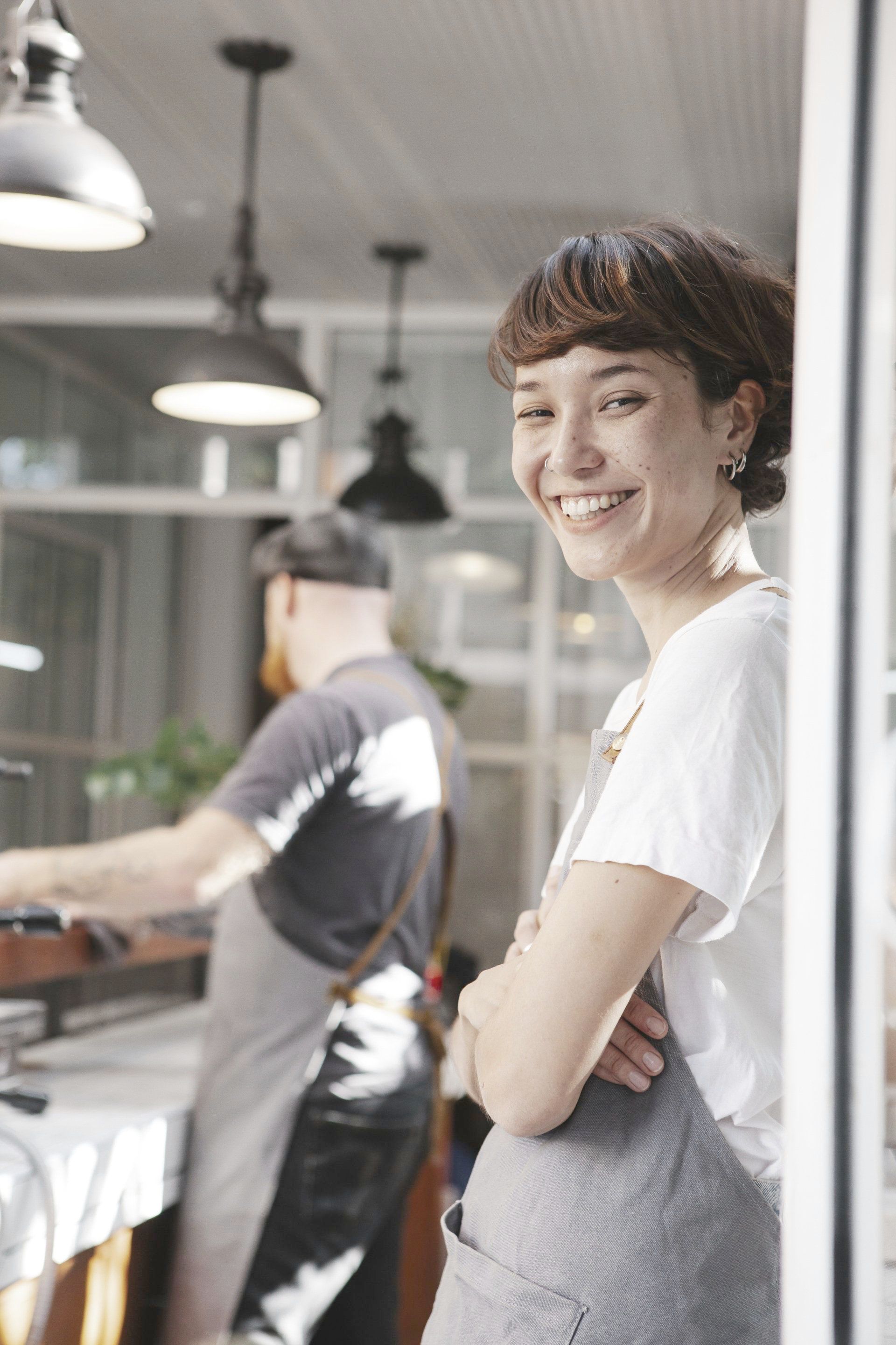 A woman is smiling while standing in front of a window in a restaurant.