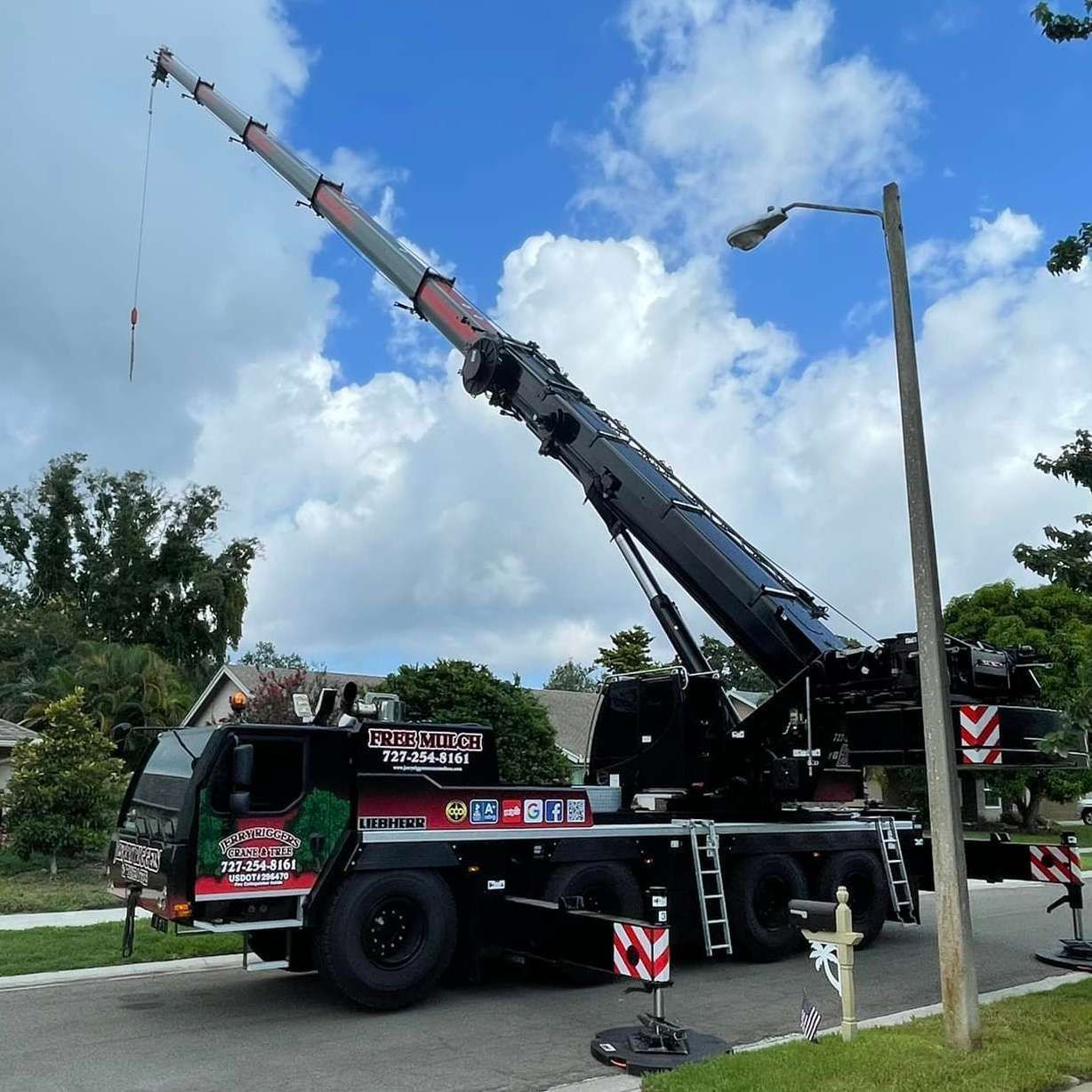 Tow truck lifting a crane boom on a roadside under a partly cloudy sky