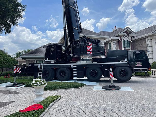 Large black crane truck parked in a suburban driveway in front of a house under a blue sky