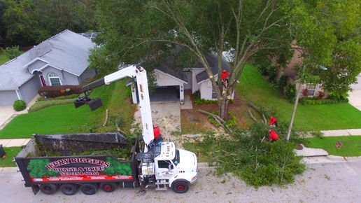 White utility truck with crane removing a large fallen tree limb from a front yard