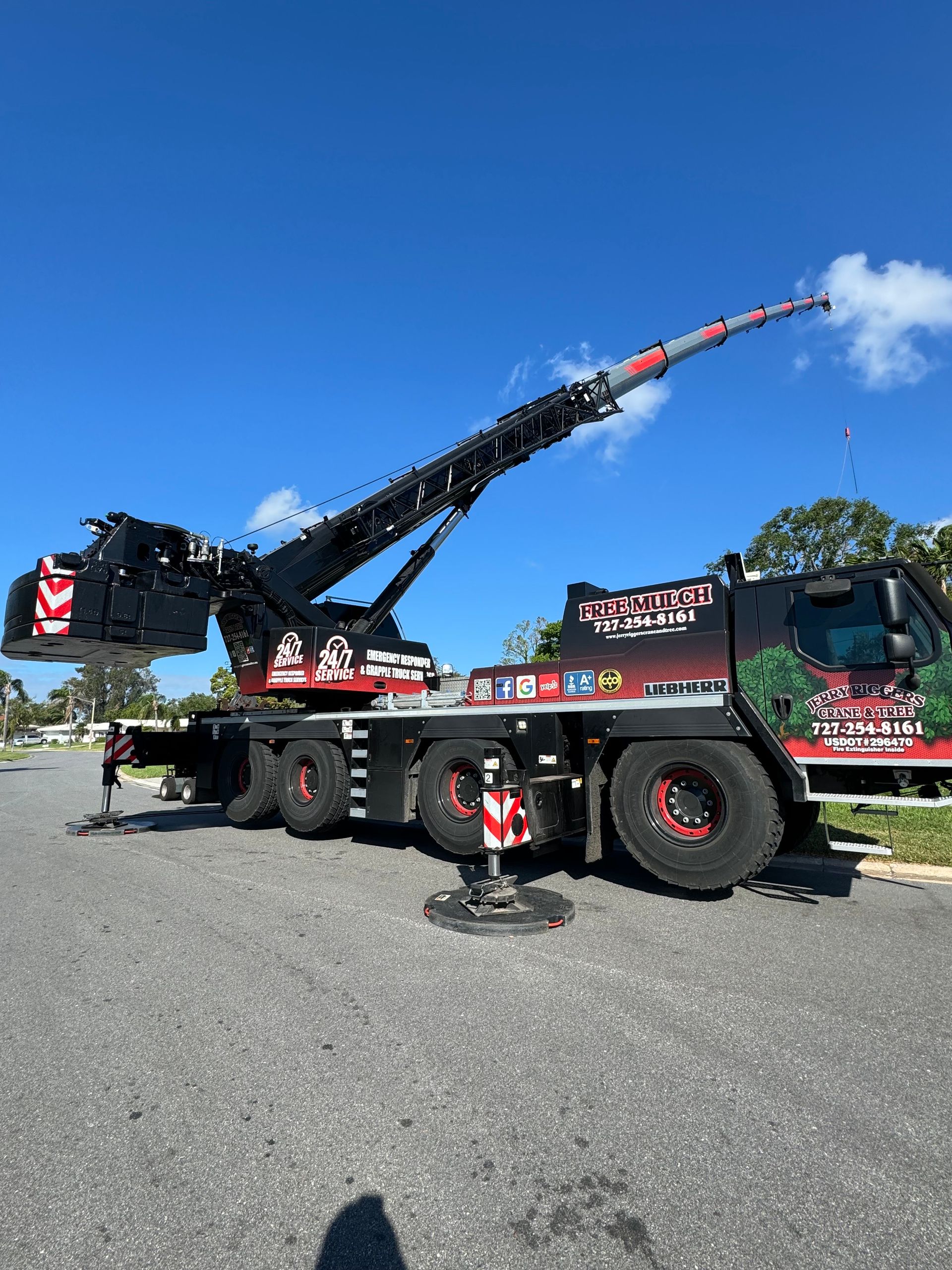 Large black and red crane truck with raised boom parked on a sunny street under a blue sky