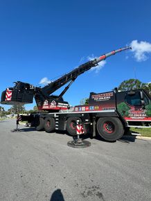 Large black and red crane truck with raised boom parked on a sunny street under a blue sky