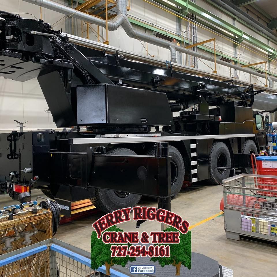 Black crane truck inside warehouse with tire racks and red shopping carts; Terry Riggs Crane & Tree sign below