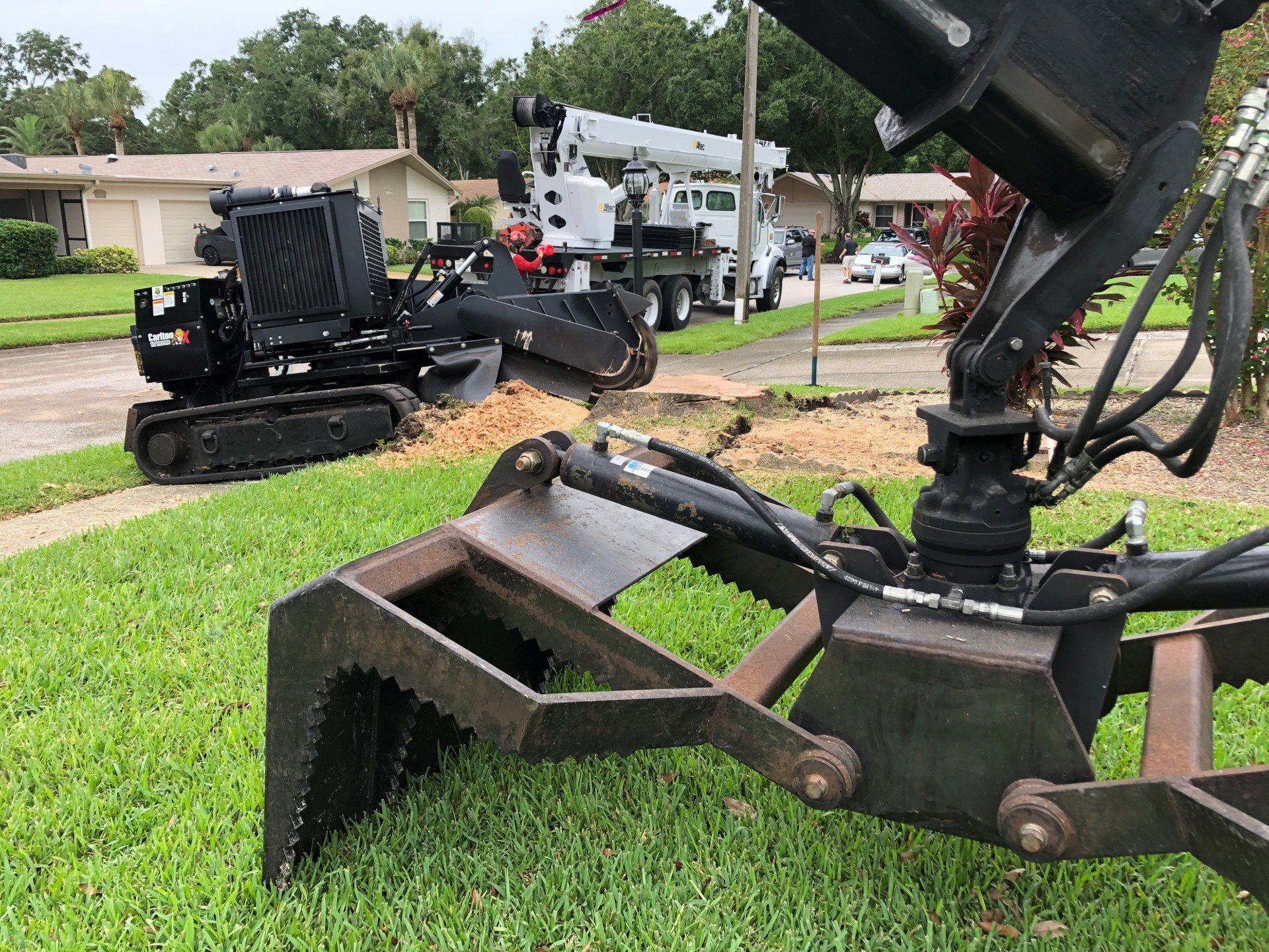 Black excavator bucket and arm over grass in a suburban neighborhood