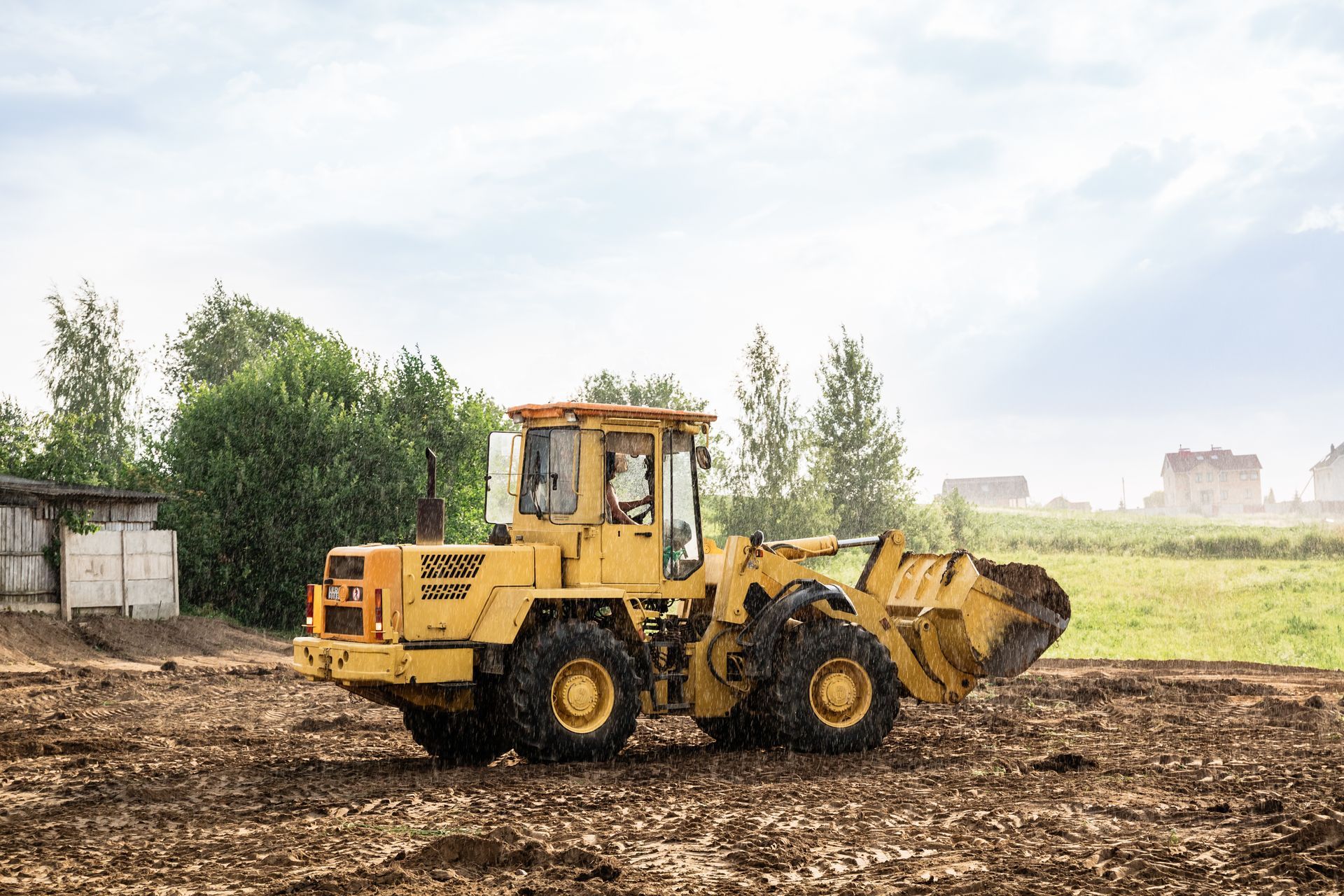 Yellow front loader on a muddy construction site with a cloudy sky in the background