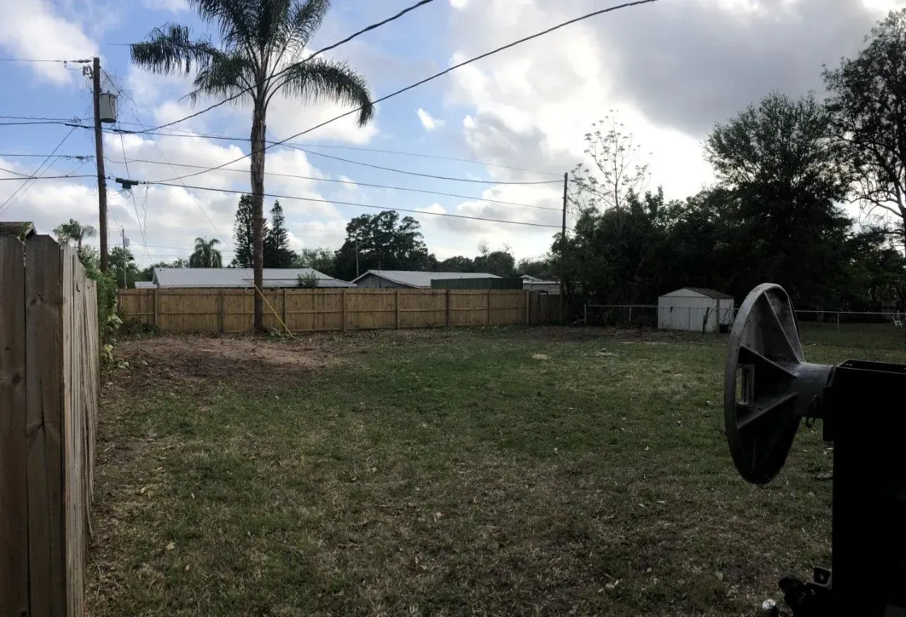 Backyard with a grassy yard, palm tree, fence, cloudy sky, and a black horn speaker in the foreground