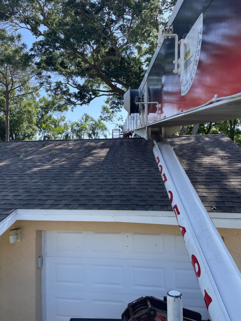 Exterior view of house roof with a red truck-mounted ladder parked beside it and trees overhead