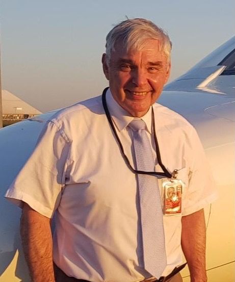 A man in a white shirt and tie is standing in front of an airplane