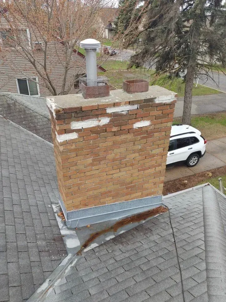 A brick chimney on top of a roof next to a white suv.
