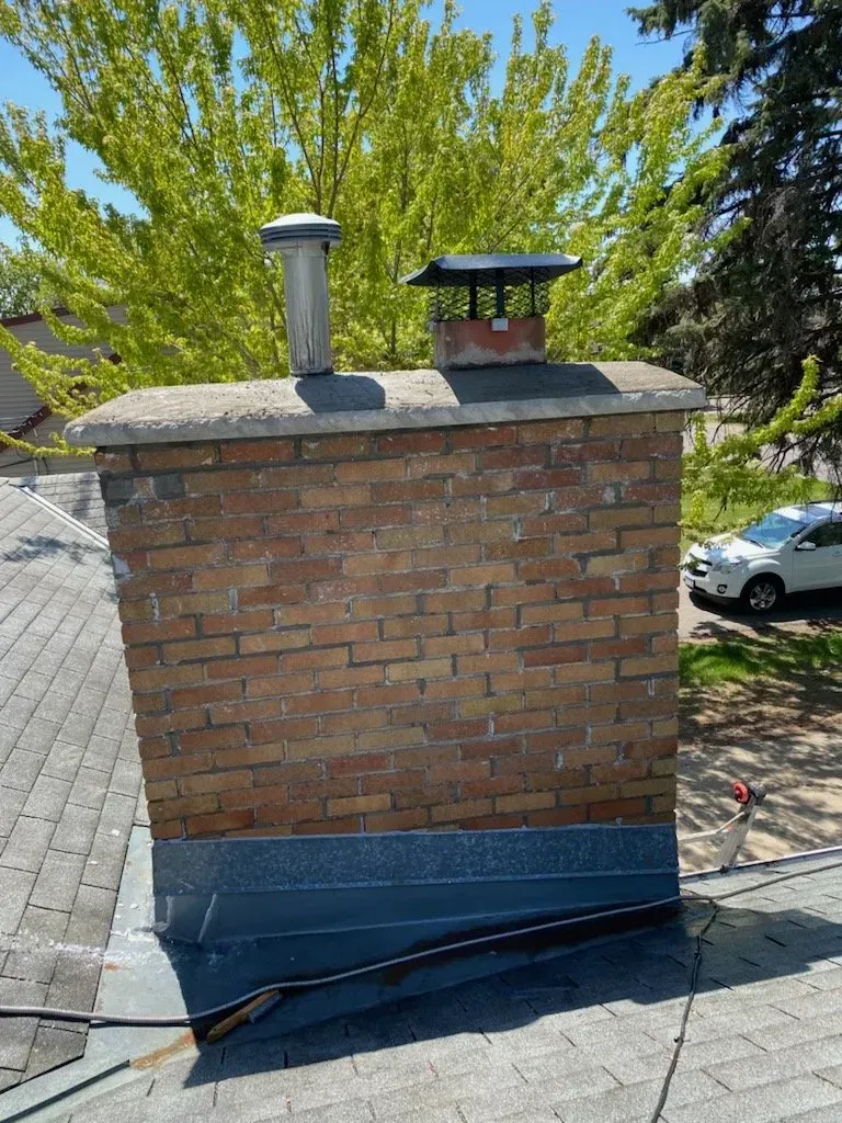 A brick chimney is sitting on top of a roof.