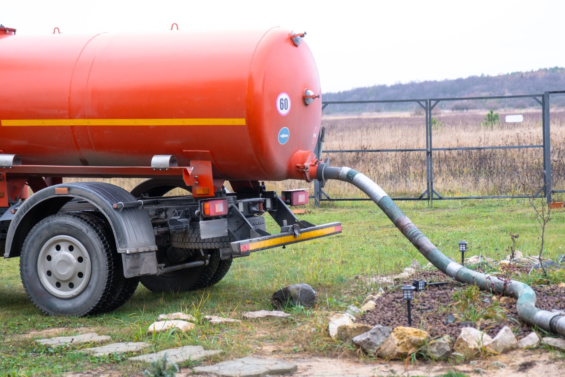 Red tanker truck pumping liquid through a large hose into a ground access point outdoors. Red tanker truck pumping liquid through a large hose into a ground access point outdoors.